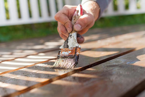 hand-holding-a-brush-applying-varnish-paint-on-wooden-surface
